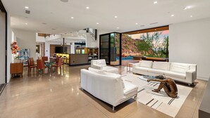 A modern living room with a large window, a dining area, and a kitchen.