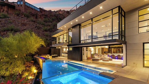 A modern house with a large swimming pool, outdoor seating, and a view of the surrounding landscape.