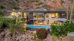 A modern two-story house with a large glass facade, a swimming pool, and a desert garden.