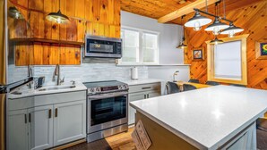 A kitchen with wooden cabinets, a stainless steel stove, a microwave, and pendant lights.