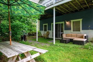 Une terrasse couverte avec une table de pique-nique, du mobilier d’extérieur et un parasol vert.