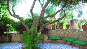 A stone-tiled patio with a tree, stone wall, and green benches.