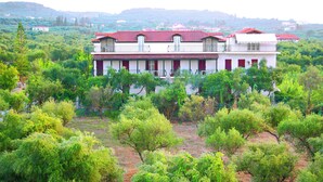 A two-story building with a red-tiled roof, surrounded by lush greenery and trees.