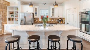 A kitchen with a large island, white cabinetry, a stone accent wall, and a built-in oven.