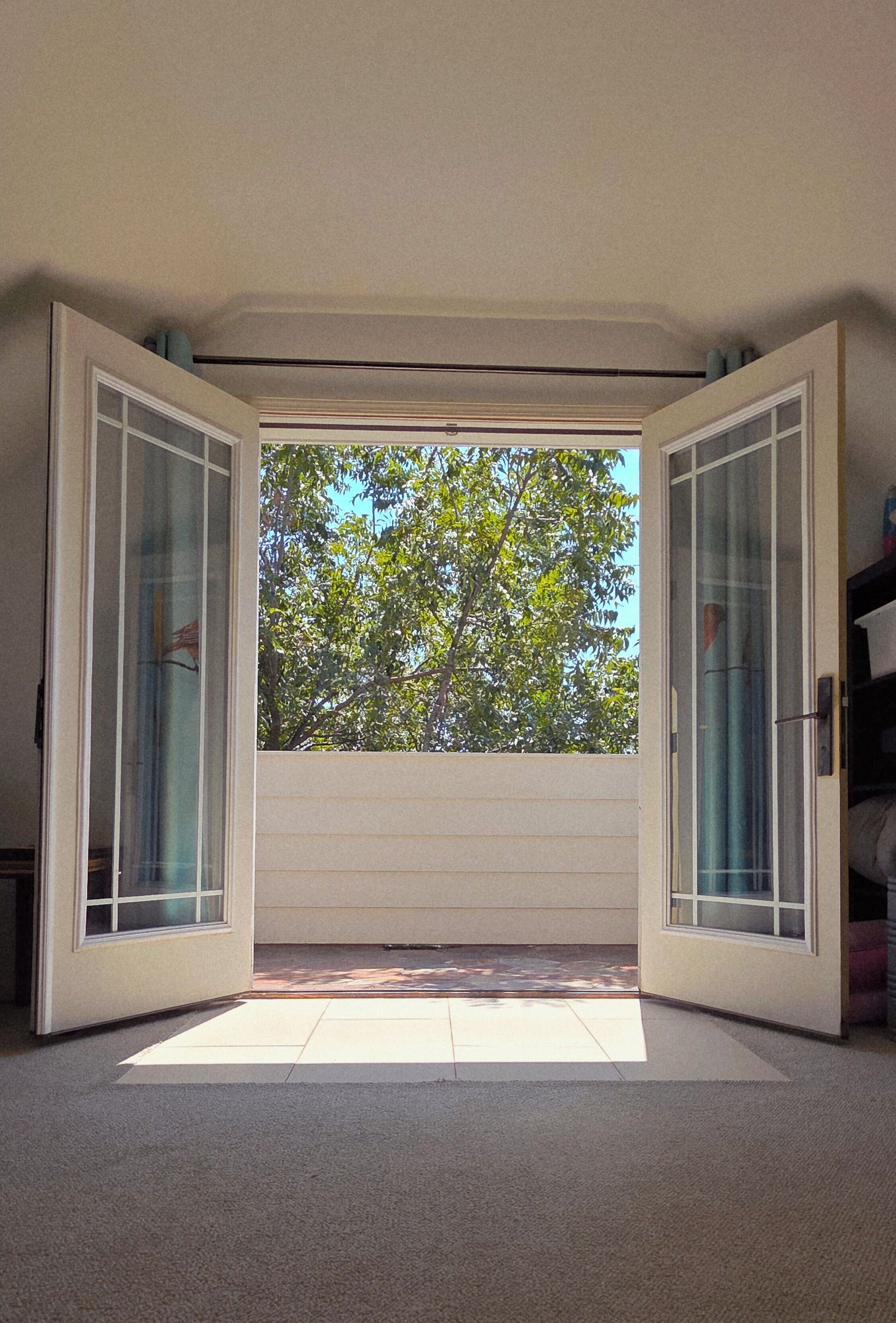 An open sliding glass door leading to a balcony with a view of trees.