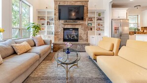 A living room with a stone fireplace, a flat-screen TV, and built-in shelving.