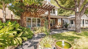 A house with a stone facade, a pergola, and a garden with a water feature.