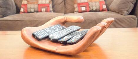 A wooden hand-shaped tray holding multiple remote controls on a wooden table.