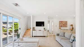 Uma sala de estar ampla com sofá, mesa de centro e TV fixada na parede.