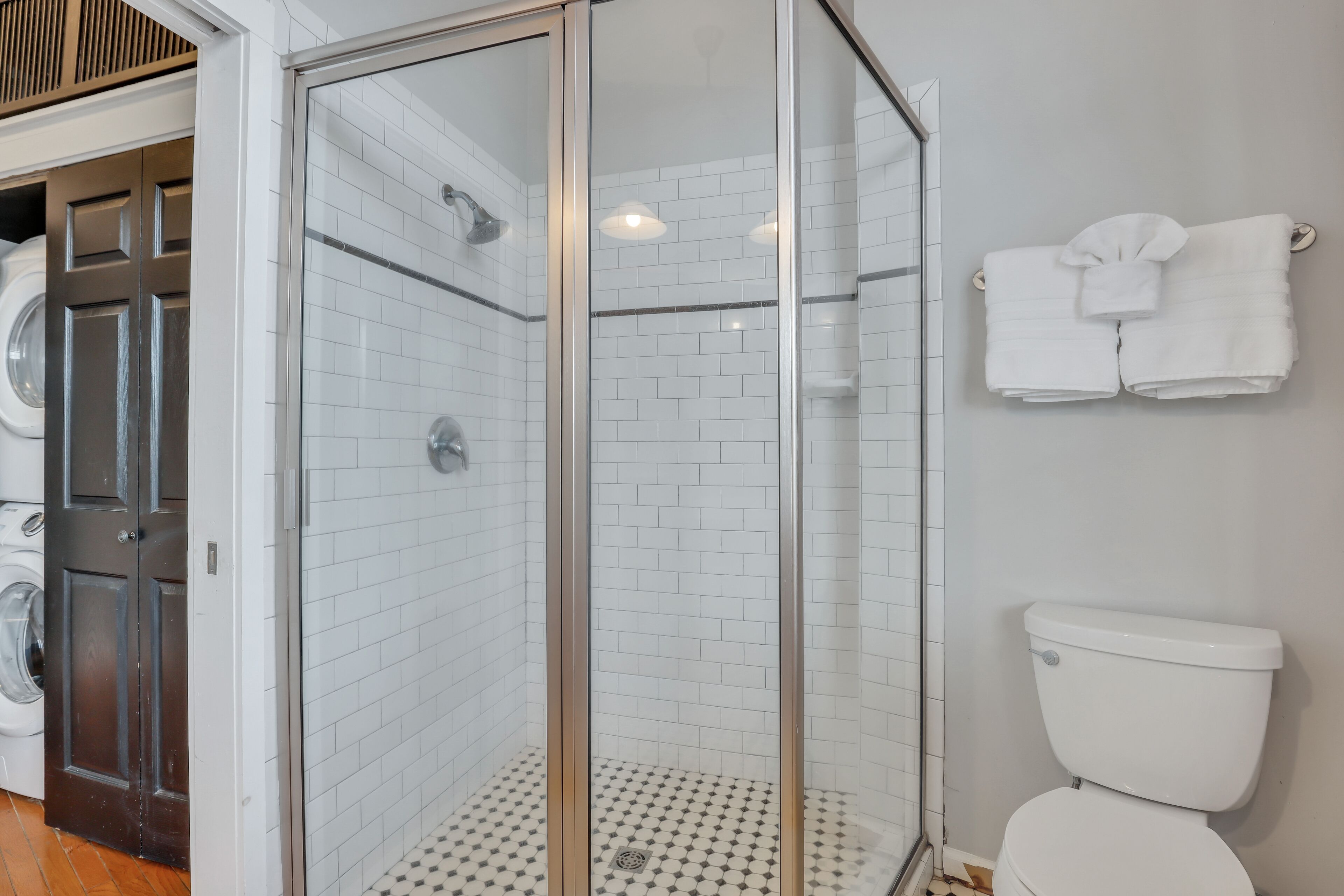 Un baño con cabina de ducha de vidrio, inodoro y lavadora.