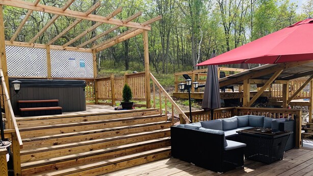 A wooden deck with a built-in grill, outdoor seating, and a red umbrella. - Peaceful house with hot tub, private swimming pool, etc.  (Albrightsville)
