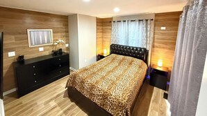 A modern bedroom with a large bed, a dresser, a TV on the wall, and a window with curtains. - Peaceful house with hot tub, private swimming pool, etc.  (Albrightsville)