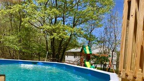 A swimming pool with a wooden deck, surrounded by trees and a play structure. - Peaceful house with hot tub, private swimming pool, etc.  (Albrightsville)