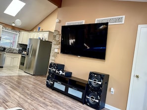 Uma sala de estar moderna com uma TV de tela plana, um móvel de entretenimento preto e uma cozinha ao fundo.