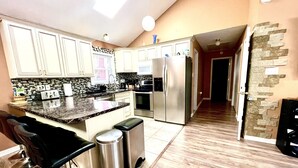 A modern kitchen with white cabinets, a granite countertop, stainless steel appliances, and a bar area with stools. - Peaceful house with hot tub, private swimming pool, etc.  (Albrightsville)