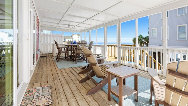 A covered outdoor deck with wooden furniture, a welcome mat, and a view of the ocean.