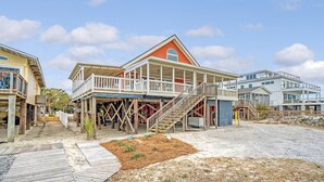 A beachfront property with a wooden deck, a covered outdoor area, and a staircase leading to a second floor.