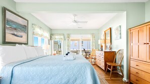 A bedroom with a large bed, a wooden dresser, a chair, and a ceiling fan.