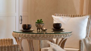 A wicker chair with a white cushion, a glass table with two dark bowls and a small plant, and a lit candle. - "La Cabane" - Private Pool (Copacabana)