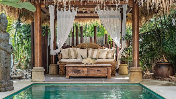 A poolside area with a wooden bench, a cushioned seating area under a canopy, and a stone statue. - "La Cabane" - Private Pool (Copacabana)