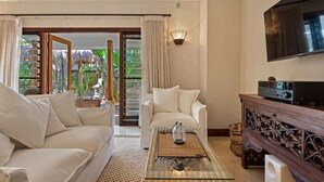 A living room with a sofa, armchair, and coffee table. There is a TV mounted on the wall and a sliding glass door leading to a balcony with a view of greenery. - "La Cabane" - Private Pool (Copacabana)