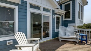 Een overdekt terras met Adirondack-stoelen en een kleine tafel, met uitzicht op een woonwijk.