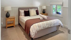 A neatly arranged bedroom with a bed, two bedside tables, and a window with a view of greenery. - River Rock Cottage  Centrally located and Dog friendly (Jamieson)