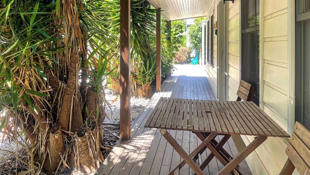 A wooden deck with a table and benches, surrounded by lush greenery and a covered porch. - River Rock Cottage  Centrally located and Dog friendly (Jamieson)