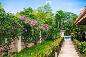 Un sentier qui mène à une piscine entourée d’une végétation luxuriante et de plantes en fleurs.
