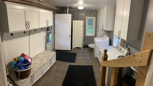 A laundry room with white cabinets, a washing machine, a sink, and a wooden chair. - Walloon Lake Cottage; Minutes Walk to Water & The Village (Walloon Lake)