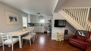 A spacious living area with a dining table, chairs, a red leather sofa, a staircase, and a kitchen in the background. - Walloon Lake Cottage; Minutes Walk to Water & The Village (Walloon Lake)