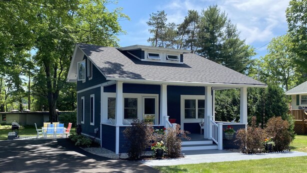A two-story house with a covered porch, a garage, and a well-maintained lawn. - Walloon Lake Cottage; Minutes Walk to Water & The Village (Walloon Lake)