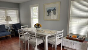 A dining area with a white table, four chairs, a vase of flowers, and a framed picture on the wall. - Walloon Lake Cottage; Minutes Walk to Water & The Village (Walloon Lake)