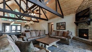 A spacious living room with a stone fireplace, leather sofas, and a wooden ceiling.