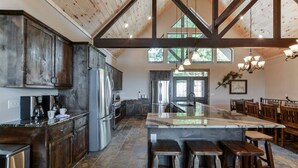 A spacious kitchen with dark wooden cabinets, a large island with stools, and a high ceiling with exposed beams.