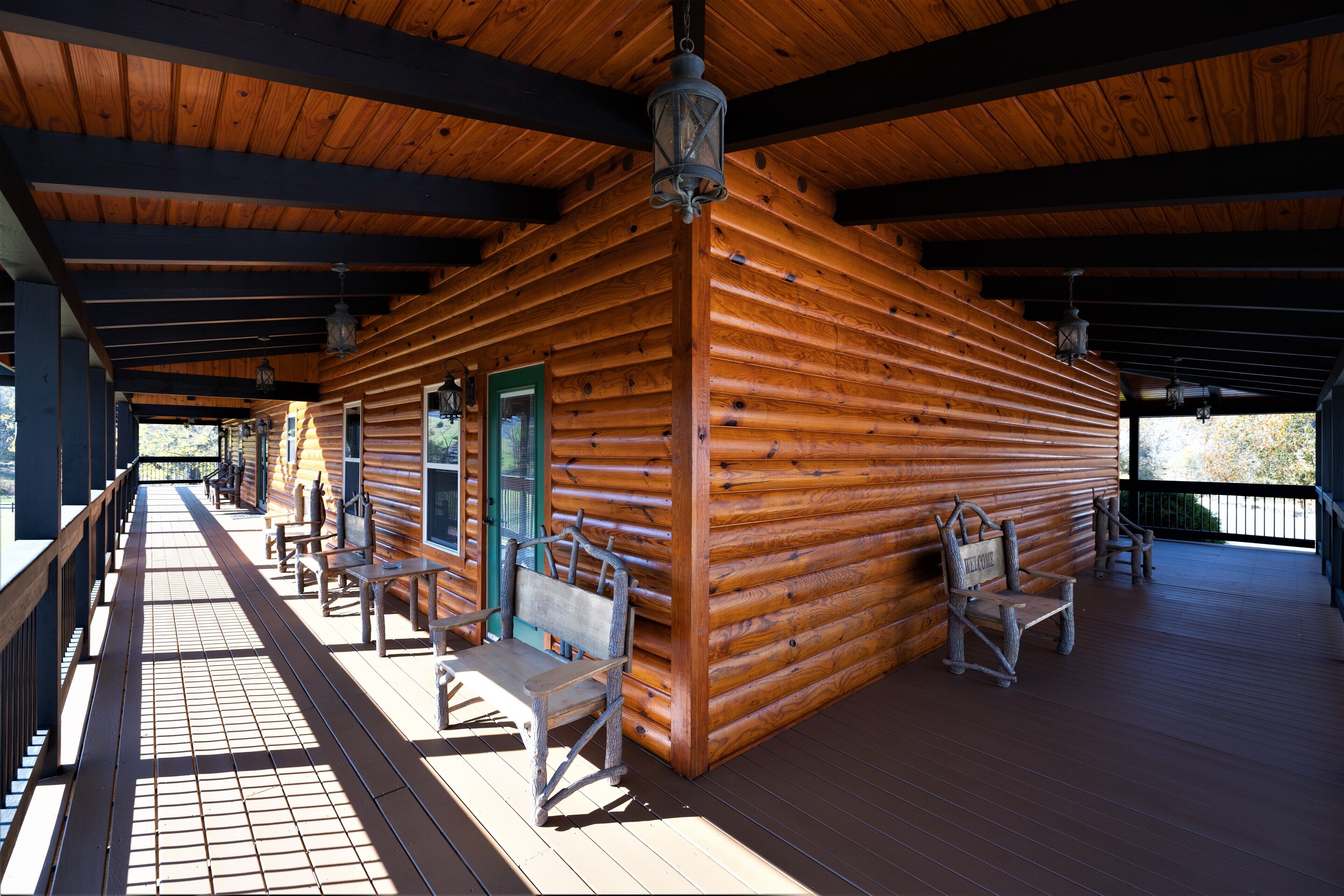 A log cabin with a porch, wooden benches, and a welcoming sign.