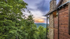 A cabin with a stone chimney, wooden exterior, and a view of a forested landscape. - Already There (Blue Ridge)