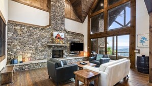 A stone fireplace, a TV, a sofa, and a large window overlooking a landscape. - Already There (Blue Ridge)