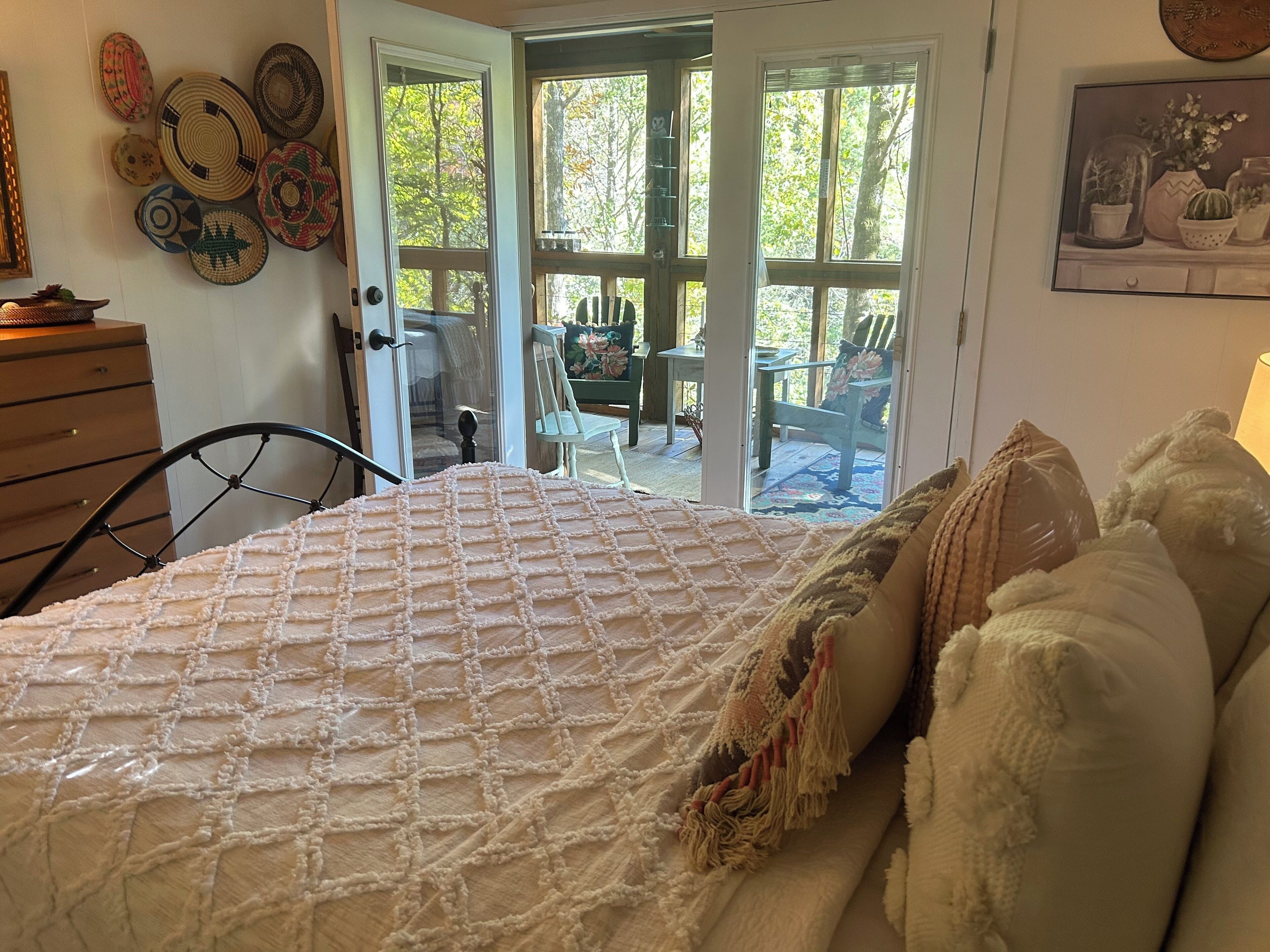 Quarto com cama, cômoda e porta para um pátio externo com mesa e cadeiras.