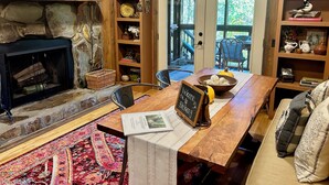 A cozy interior with a stone fireplace, wooden shelves with decorative items, a wooden table with a welcome sign, and a view of the outdoors through glass doors.