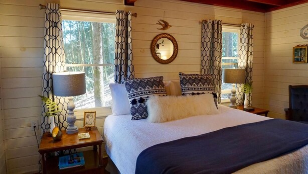 A cozy bedroom with a large bed, patterned curtains, and a wooden ceiling.