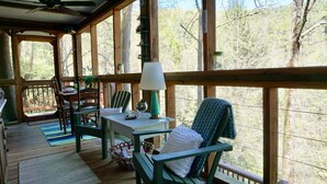 A wooden deck with a table and chairs, a lamp, and a view of trees.