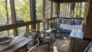 A cozy cabin with a wooden deck, a dining area with a table and chairs, and a bedroom with a bed and pillows.