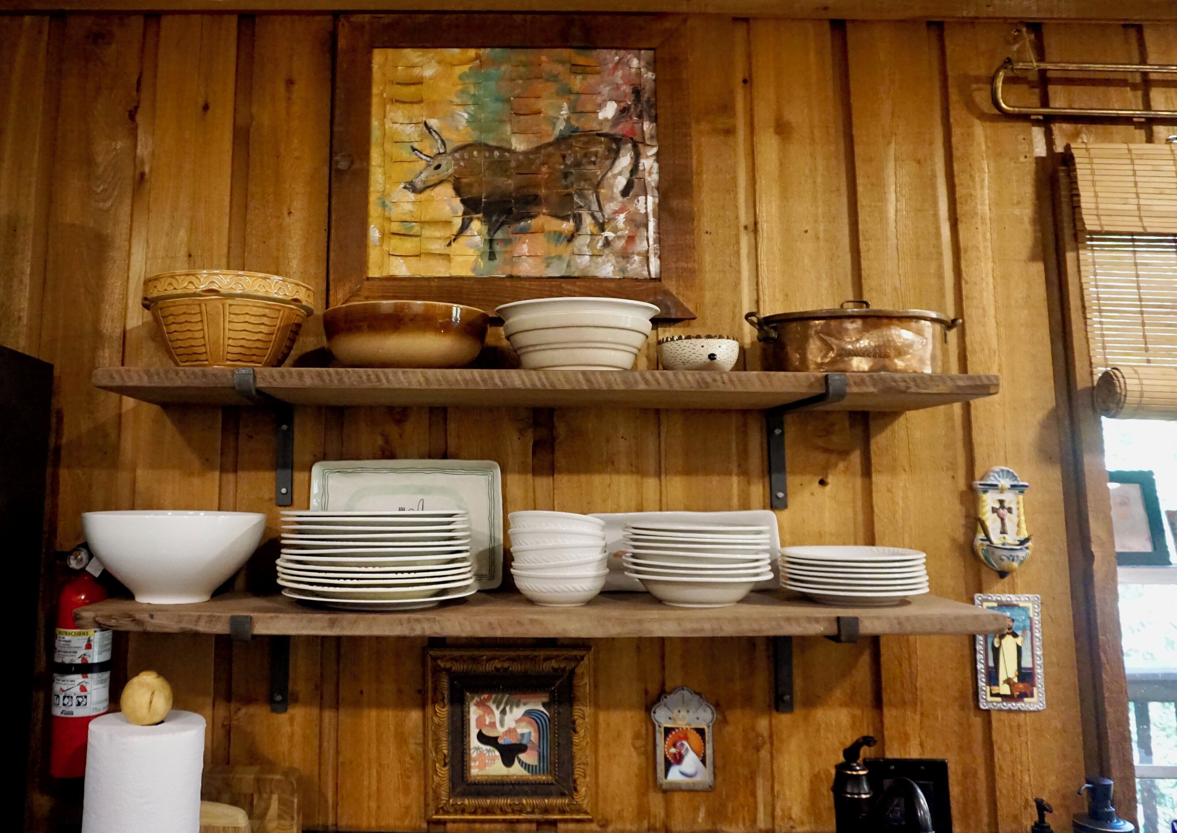 A kitchen with wooden shelves holding plates, bowls, and a decorative painting of a deer.