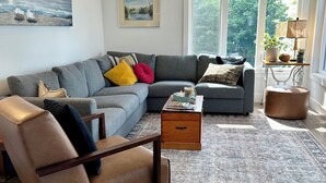 Un salon moderne avec un canapé d’angle gris, un fauteuil en cuir, une table basse en bois et un tapis à motifs.