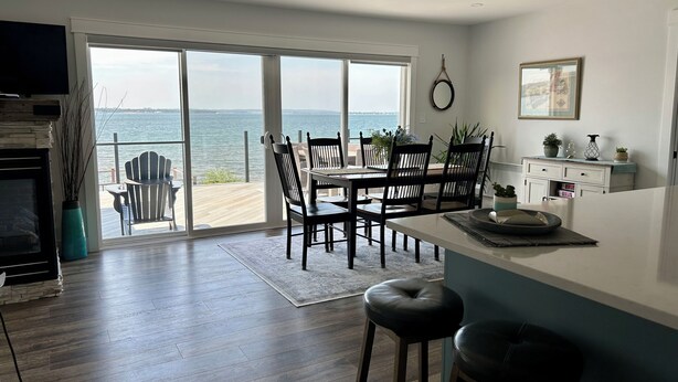 Une cuisine moderne dotée d’un grand îlot central, d’un coin repas avec des chaises et offrant une vue sur la mer grâce à de grandes fenêtres.