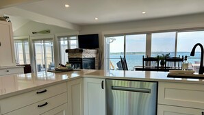 Une cuisine moderne avec des meubles blancs, un lave-vaisselle et une vue sur un lac grâce à de grandes fenêtres.