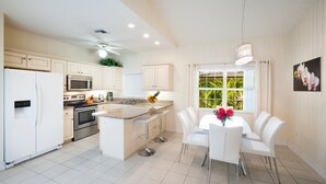 A modern kitchen with white cabinetry, a central island, and a dining area with white chairs. - Regal Beach Club #633 (Seven Mile Beach)