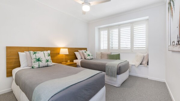 A hotel room with two beds, a ceiling fan, a window with blinds, and a painting on the wall. - RESORT ACCOMMODATION, PERFECT FOR YOUNG FAMILIES (Noosaville)