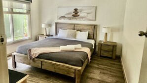 Une chambre à coucher avec un lit en bois, deux tables de chevet avec des lampes, une fenêtre avec des stores et un appareil de climatisation.